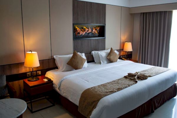 A well-decorated hotel room with a large bed, bedside tables, lamps, a wall-mounted decoration, and curtains covering a window.