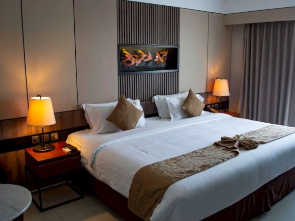 A well-decorated hotel room with a large bed, bedside tables, lamps, a wall-mounted decoration, and curtains covering a window.