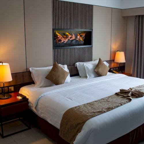 A stylish hotel bedroom featuring a large bed with white linens, bedside tables with lamps, and a wall-mounted decorative frame.