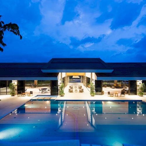 A luxurious, modern building with an inviting pool area illuminated at night, featuring outdoor seating and surrounded by a serene environment.