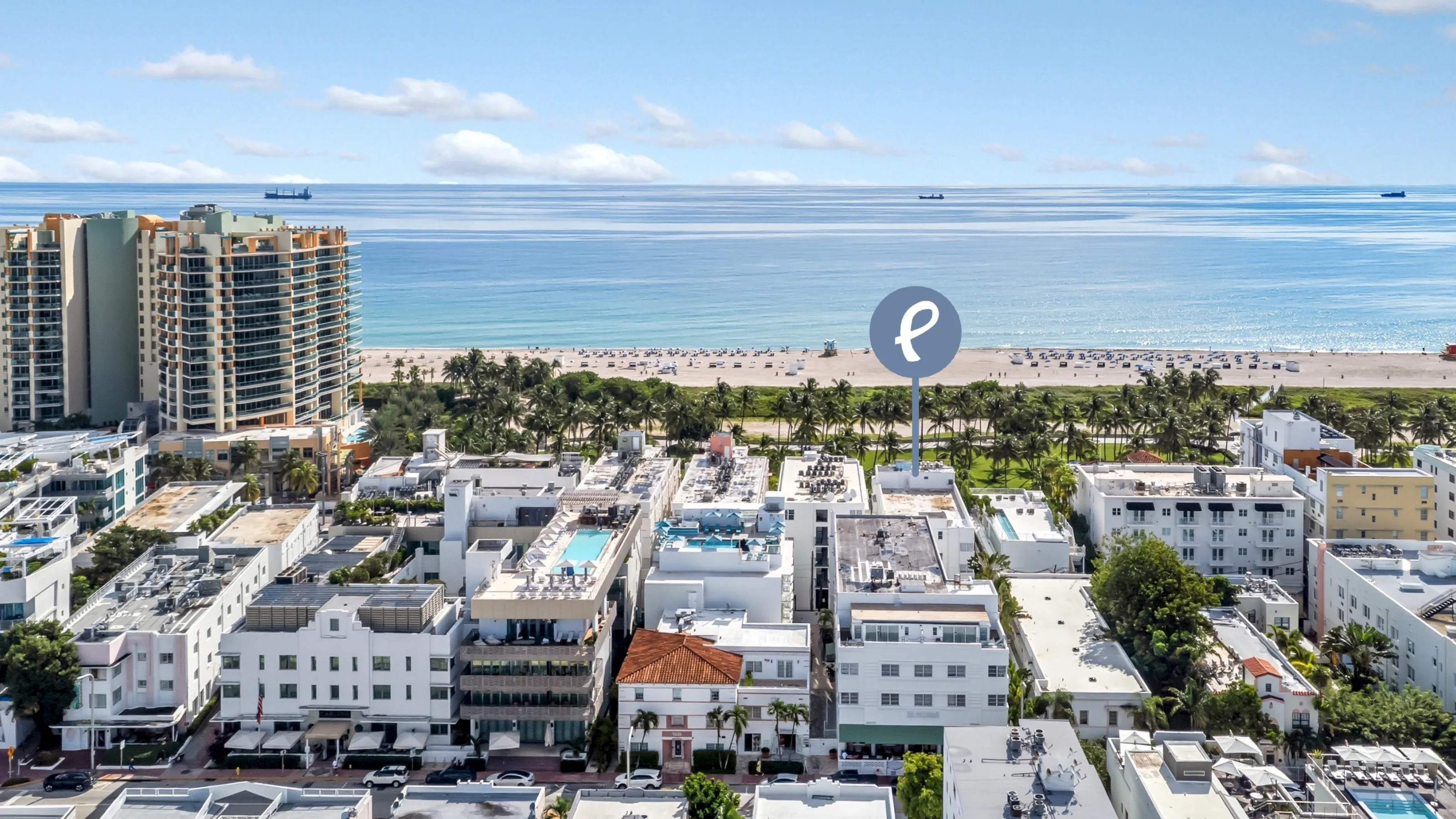Aerial view of a beachfront cityscape with white buildings, palm trees, and a large body of water.