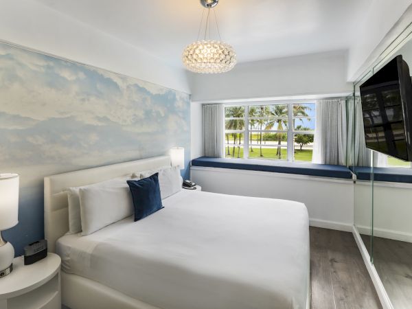 A modern bedroom with a double bed, lamps on nightstands, a wall-mounted TV, a scenic mural, large windows, and a garden view.
