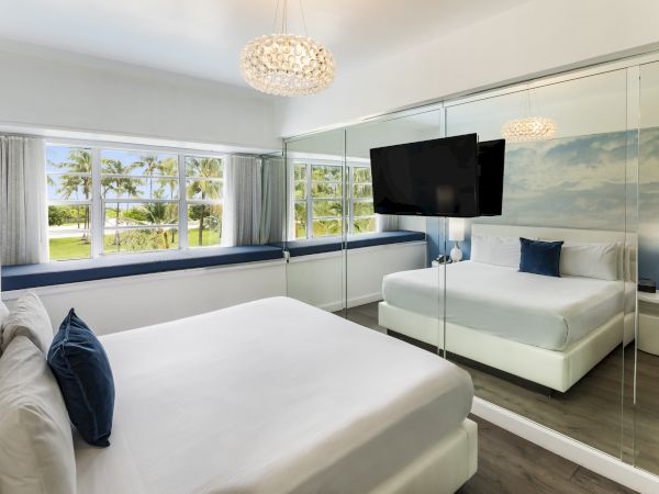 The image shows a modern bedroom with large windows, a mirrored wall, a TV, two beds, and neutral decor with blue accents and scenic outdoor views.