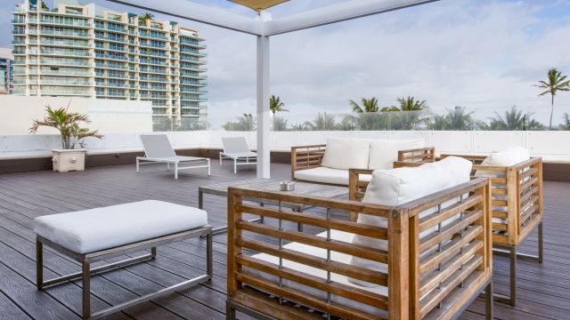 A rooftop pool area with wooden furniture and a city view.