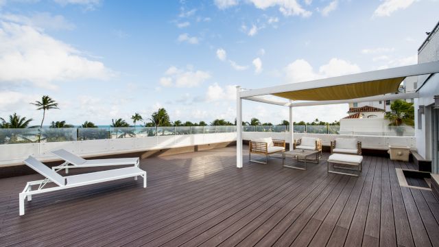 A rooftop pool area with deck, furniture, and palm trees
