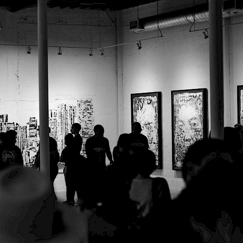 A group of people in a dimly lit gallery observes large framed artworks on the walls, creating a vibrant and thought-provoking atmosphere.