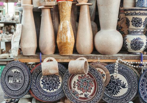 A display of pottery and ceramic items, including vases, decorated plates, and bowls, arranged on shelves at a market stall.