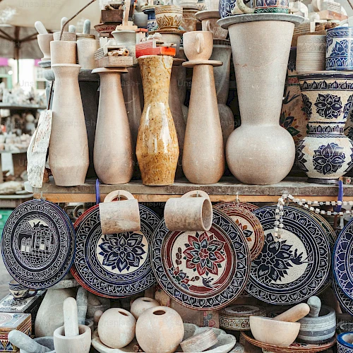 A display of pottery and ceramic items, including vases, decorated plates, and bowls, arranged on shelves at a market stall.
