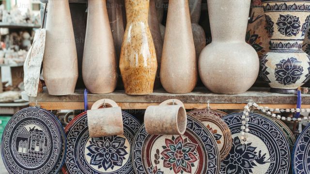A display of pottery and ceramic items, including vases, decorated plates, and bowls, arranged on shelves at a market stall.