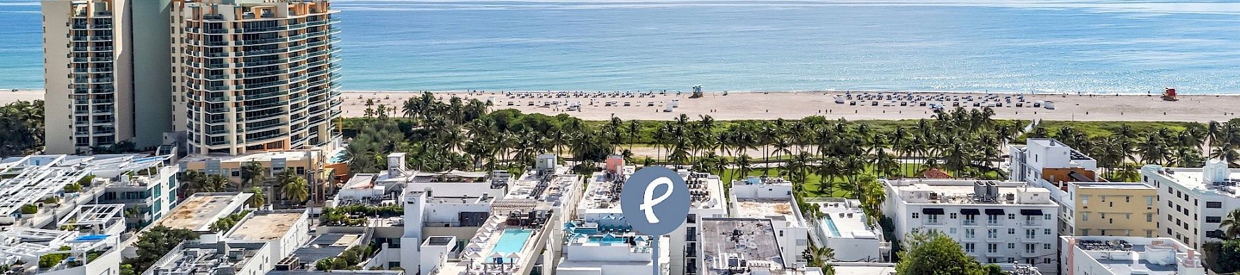 Aerial view of a beachfront hotel complex with palm trees, a sandy shore, calm blue ocean, and small boats on the horizon.