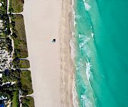 Aerial view of a beachfront resort beside a long sandy shore, with turquoise ocean waves rolling in.
