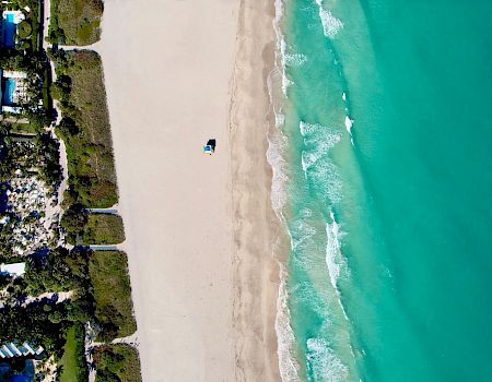 Aerial view of a beachfront resort beside a long sandy shore, with turquoise ocean waves rolling in.