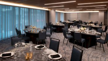 The image shows an elegantly set dining room with round tables and cushioned chairs, ready for an event.