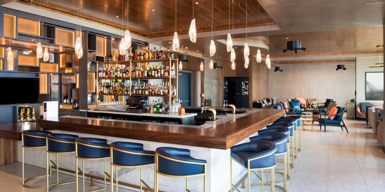 A modern bar with stylish seating, pendant lights, a well-stocked bar area, and a comfortable lounge area in the background ends the sentence.