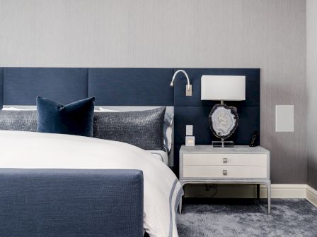 A modern bedroom with a navy blue and white color scheme, featuring a neatly made bed, a nightstand with a lamp, and a decorative stone.