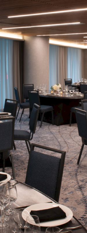 This image shows a modern, elegant banquet hall setup with round tables, black chairs, silverware, and floral centerpieces, under soft lighting.